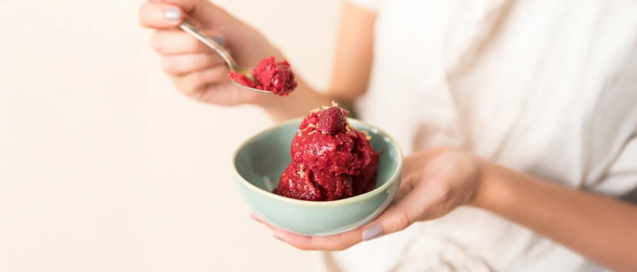 A person holding a light blue bowl of vibrant red raspberry sorbet, taking a spoonful.