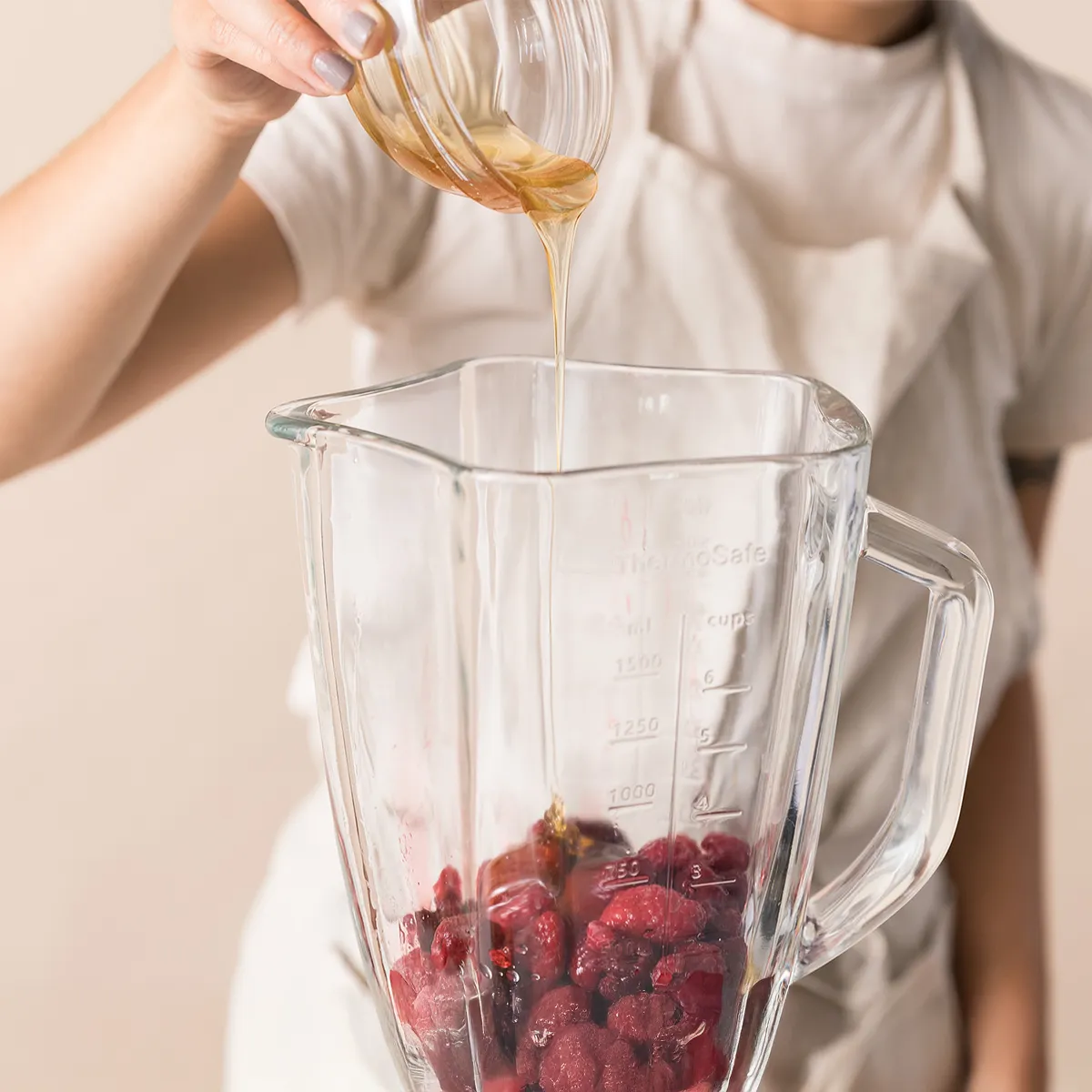 Blended raspberries being poured from a blender into a glass bowl to make homemade raspberry sorbet
