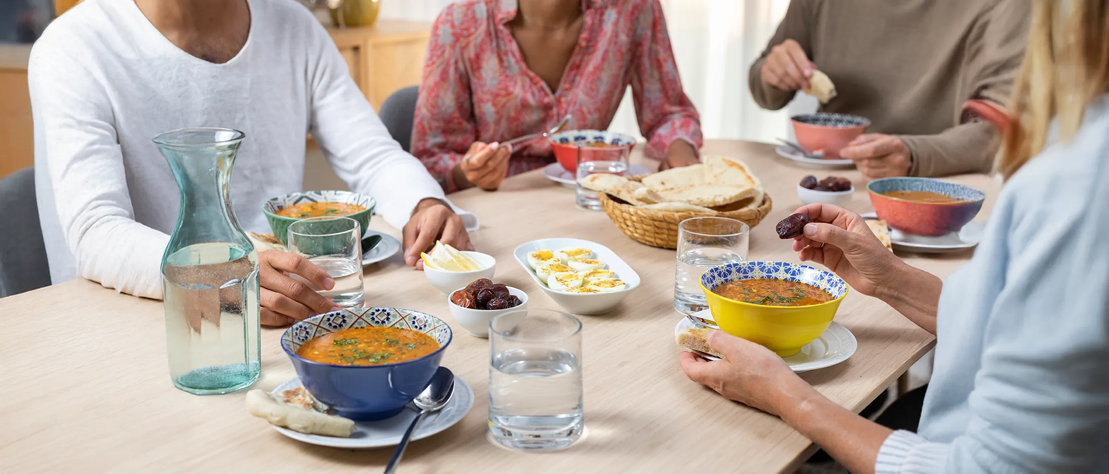  Several people seated around a table sharing bowls of orange soup 