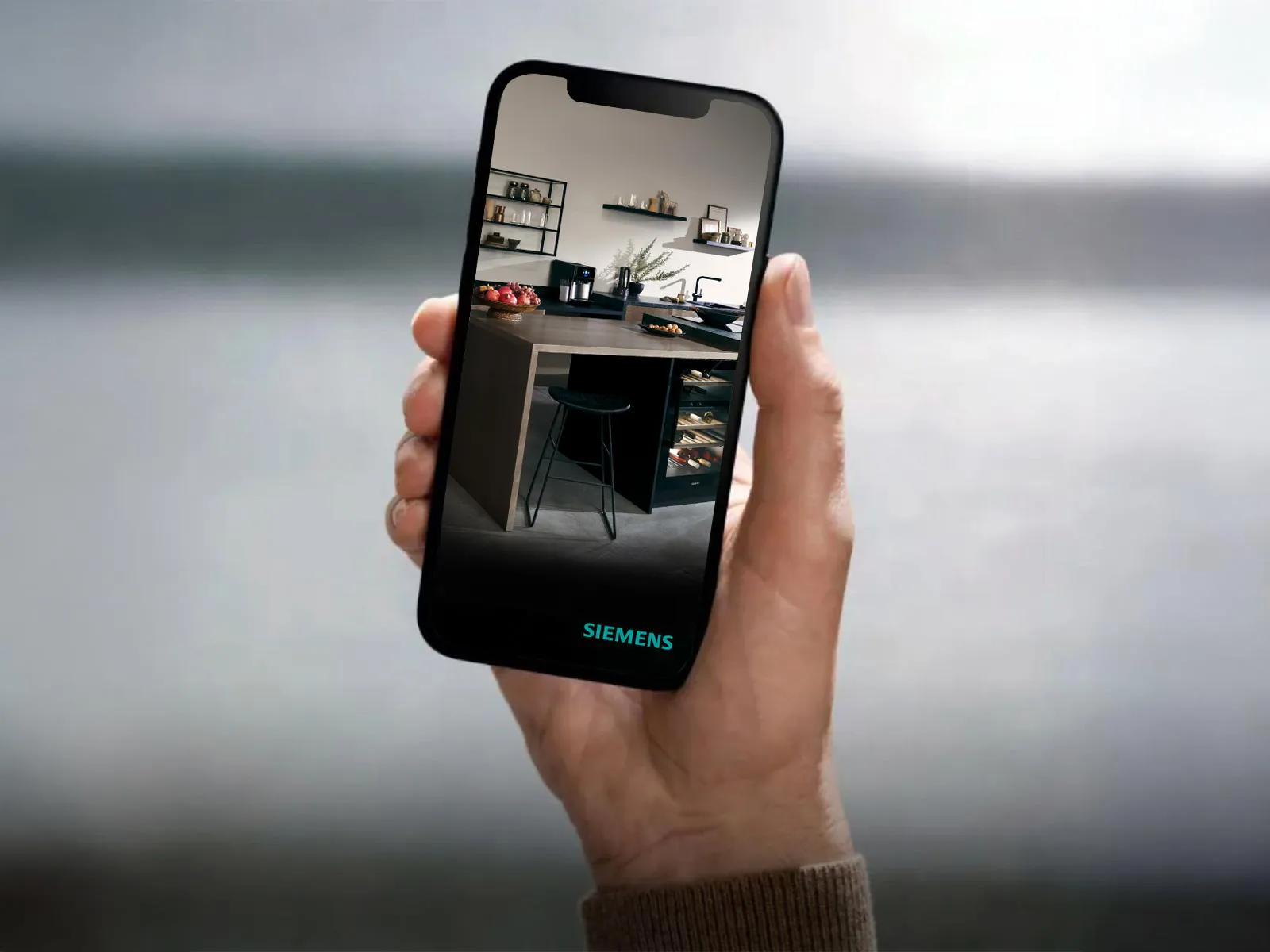 Osoba trzyma smartfon, na którym wyświetla się nowoczesna kuchnia Siemens z eleganckimi urządzeniami na tle jasnego drewna.