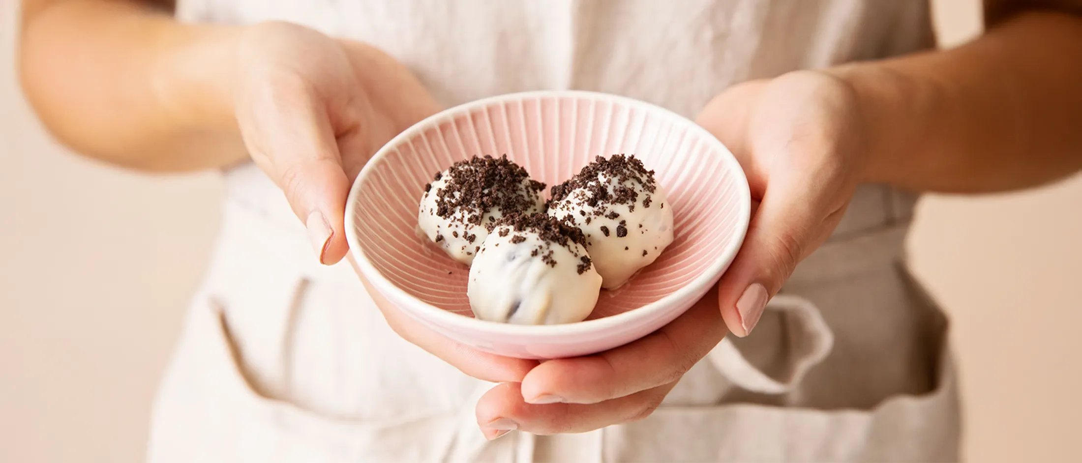 Person holding a small pink bowl with three white chocolate truffles topped with crushed cookie crumbs.