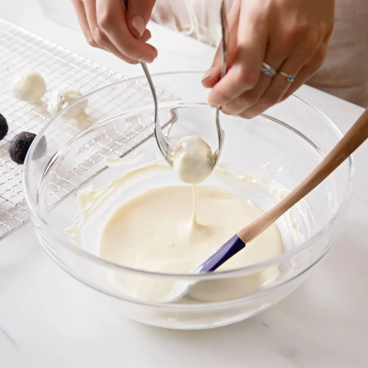 Hand dipping cookie truffle balls into melted white chocolate and placing them on a wire rack to set