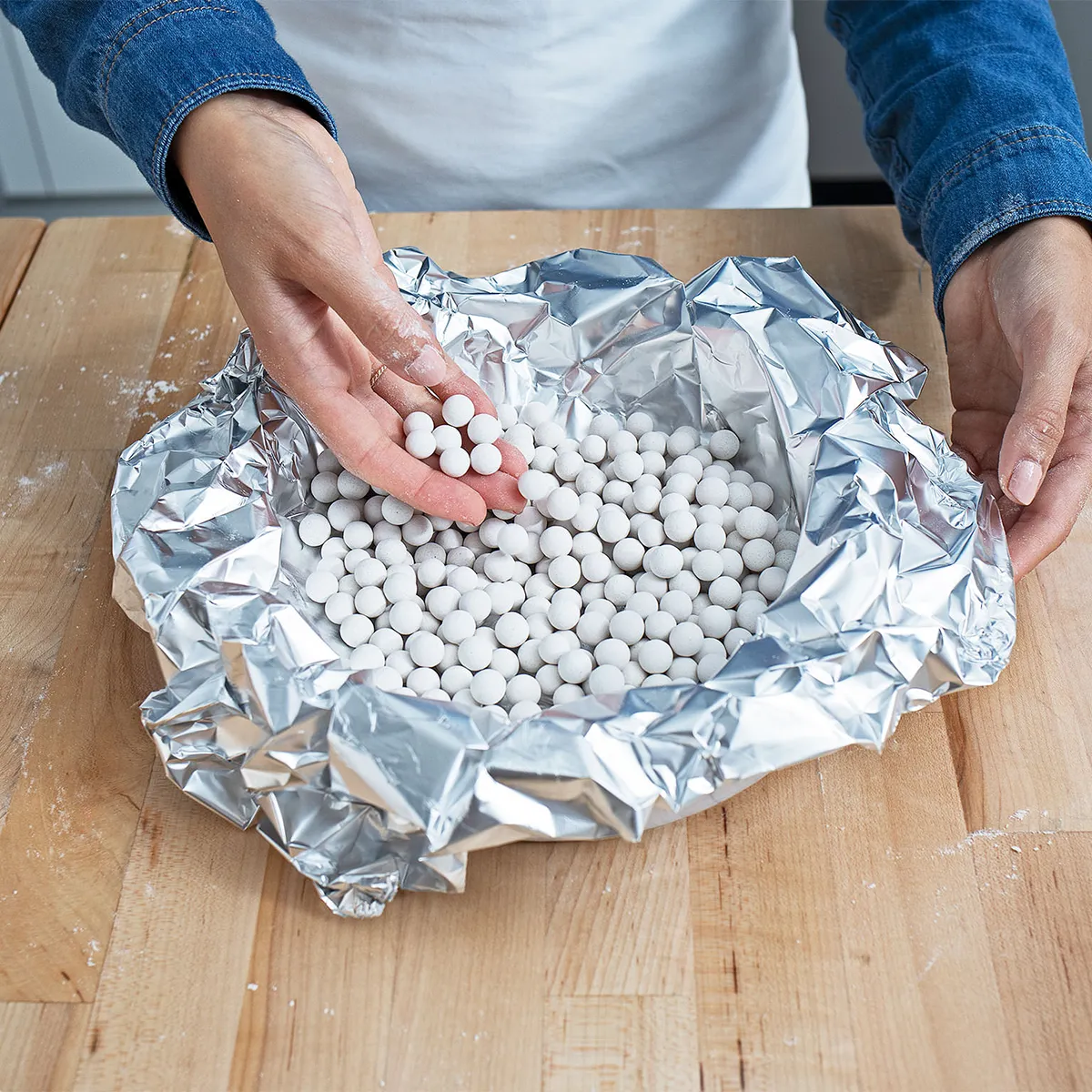 Hands placing pie weights on greased foil-lined crust to blind-bake a chocolate pecan pie shell