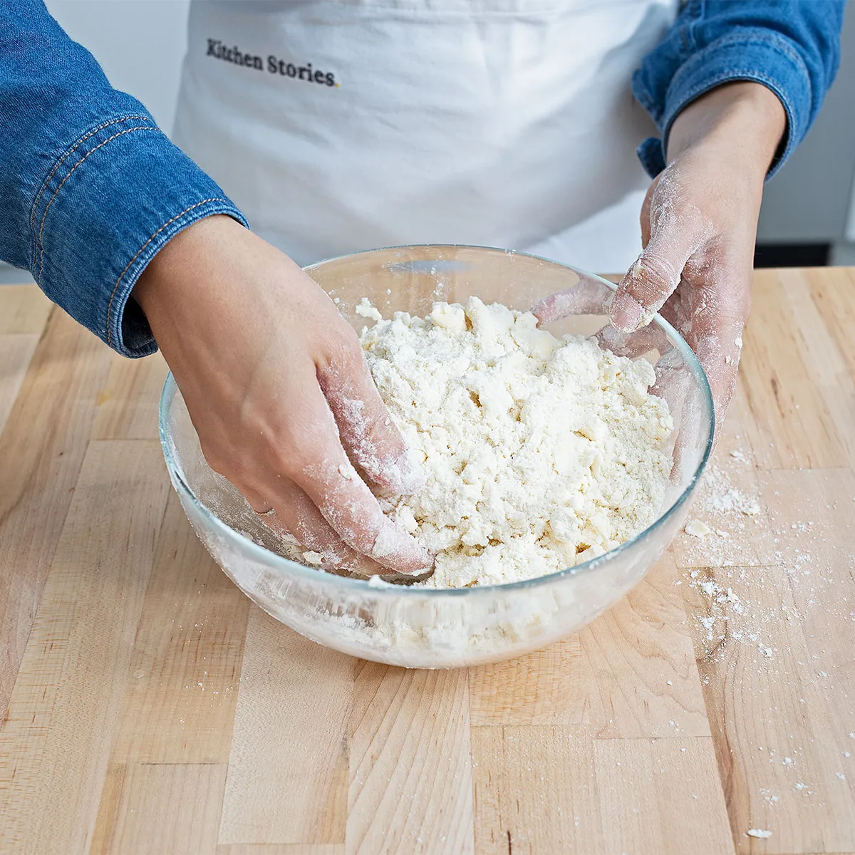 Hands holding a plastic-wrapped pie dough disk on a floured wooden board