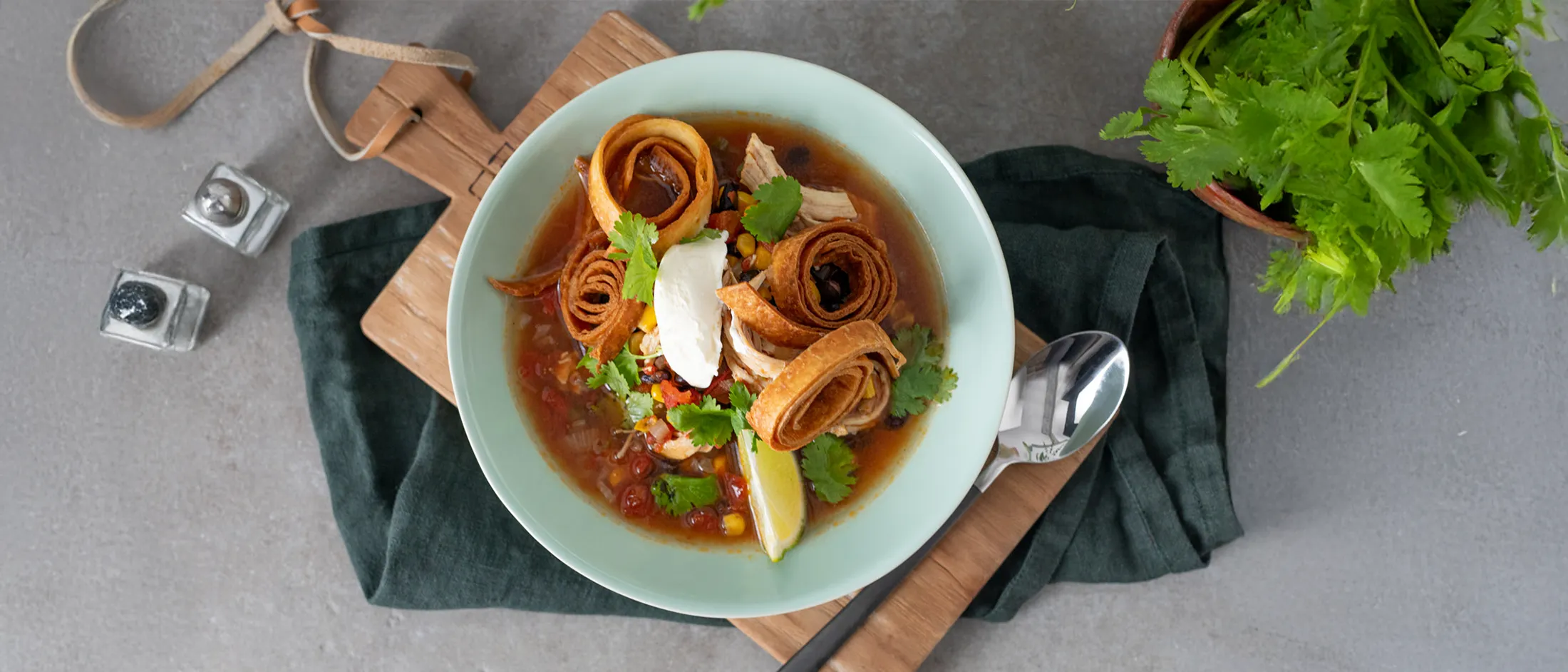 Hearty soup with meat, vegetables, and tortilla strips, garnished with cilantro and lime.