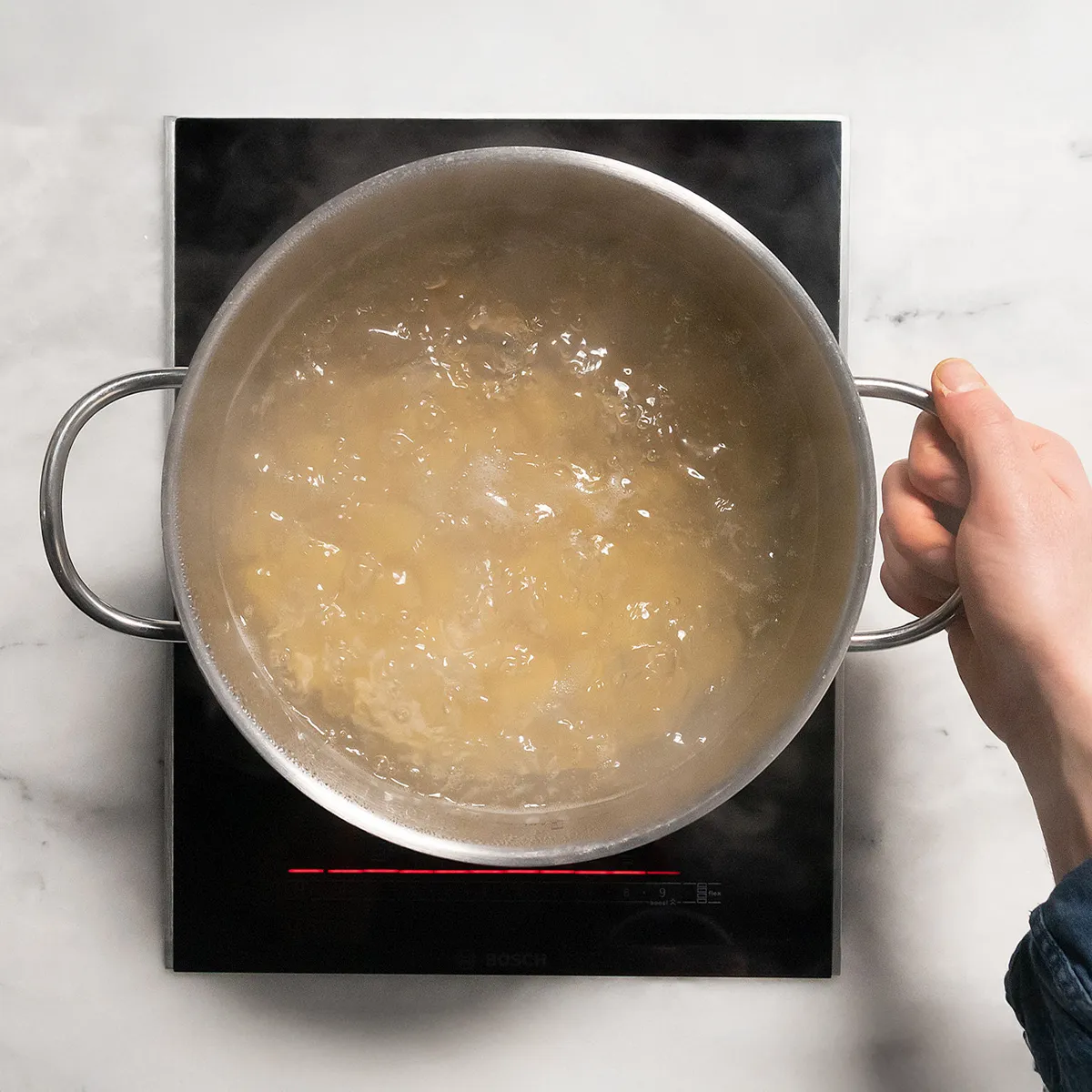 Hand holding a pot with boiling water on an induction cooktop.