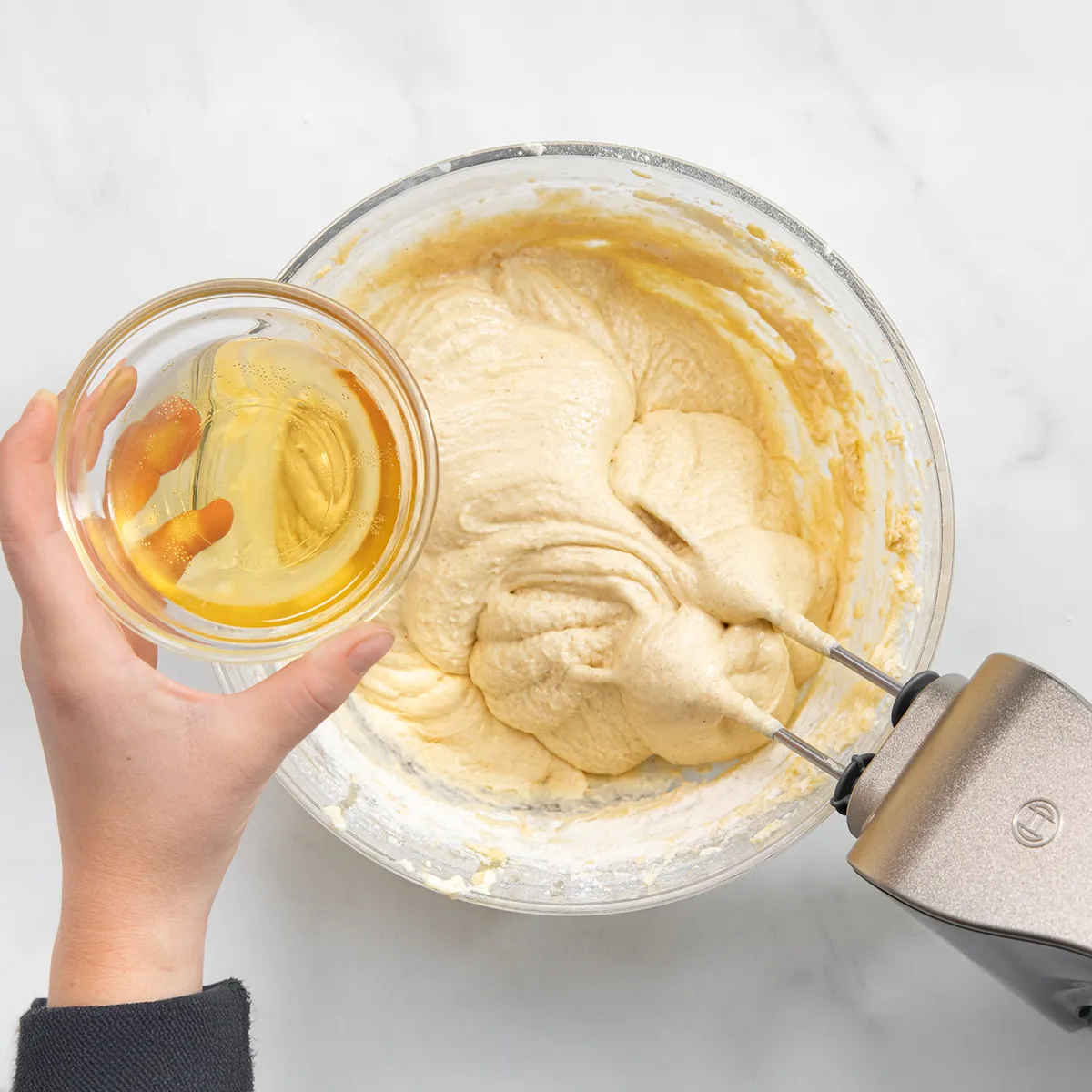 Person pouring apple cider into a mixing bowl with dry ingredients to make baked apple cider donut batter