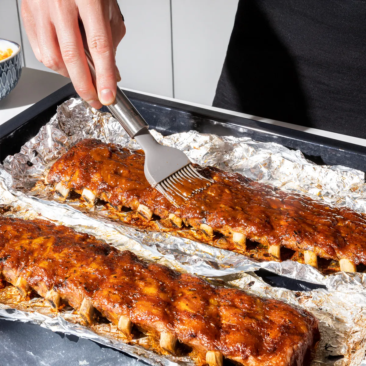 Two racks of seasoned, cooked ribs on aluminum foil inside an open stainless steel oven.