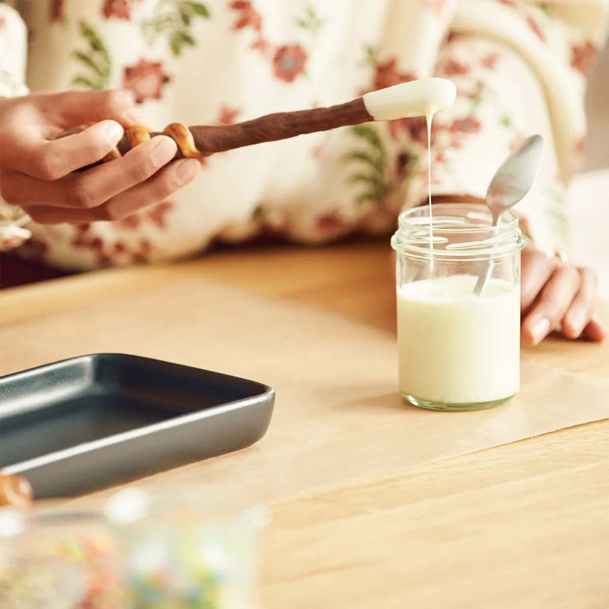 Hand dipping a chocolate-covered pretzel wand into a jar of melted white chocolate.