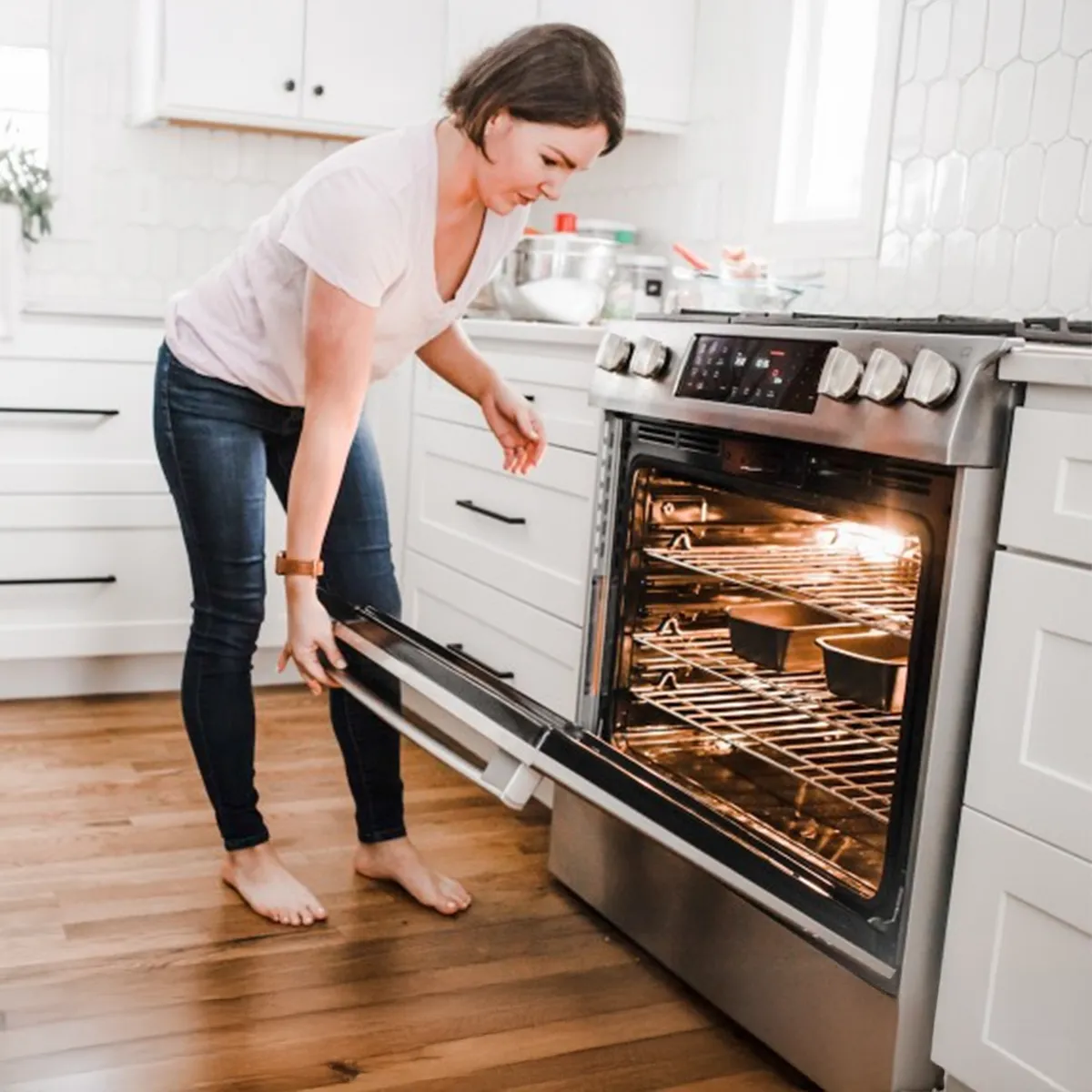 Woman placing banana bread pans into an oven in a bright kitchen while baking at home.