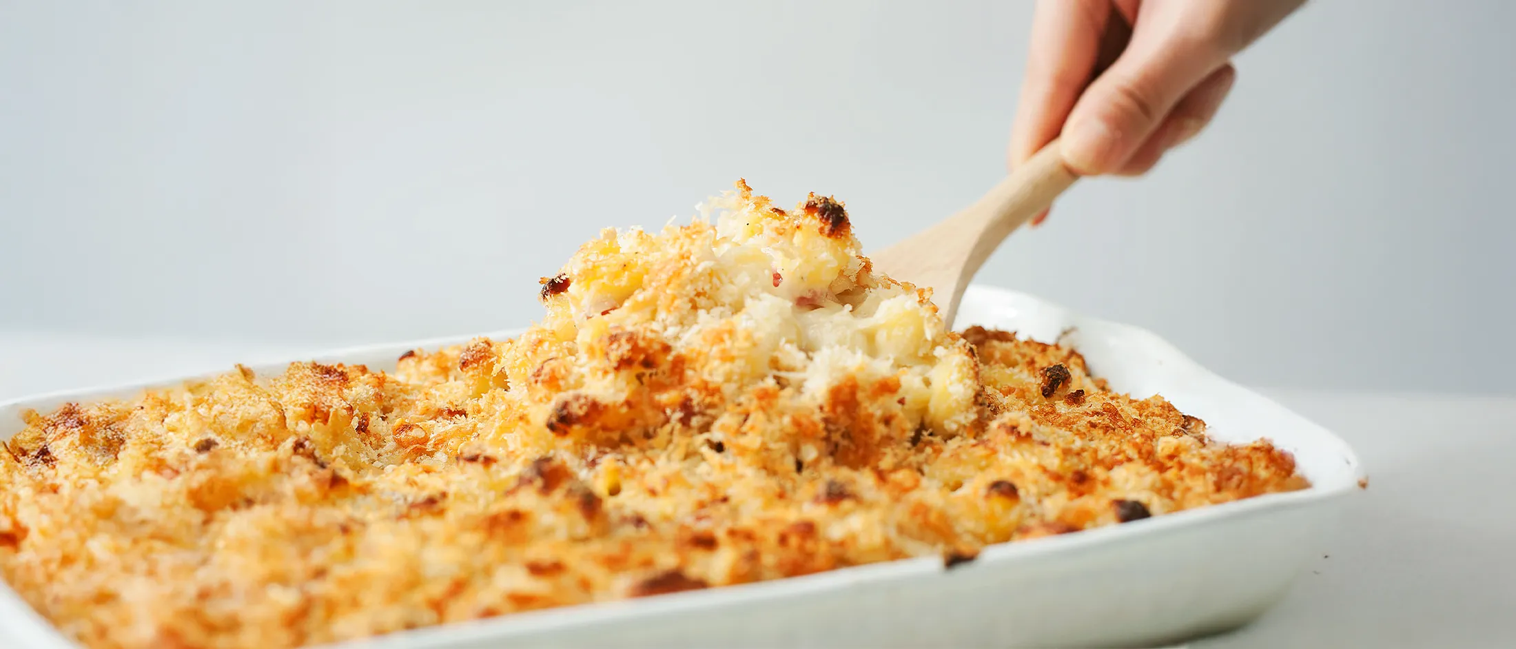 Baked macaroni and cheese casserole with a golden breadcrumb topping being served with a wooden spoon.
