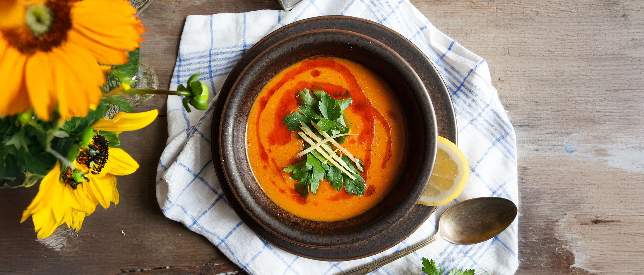 Rustic brown plates on a blue-checkered napkin with a lemon wedge, and yellow flowers on a wooden table.