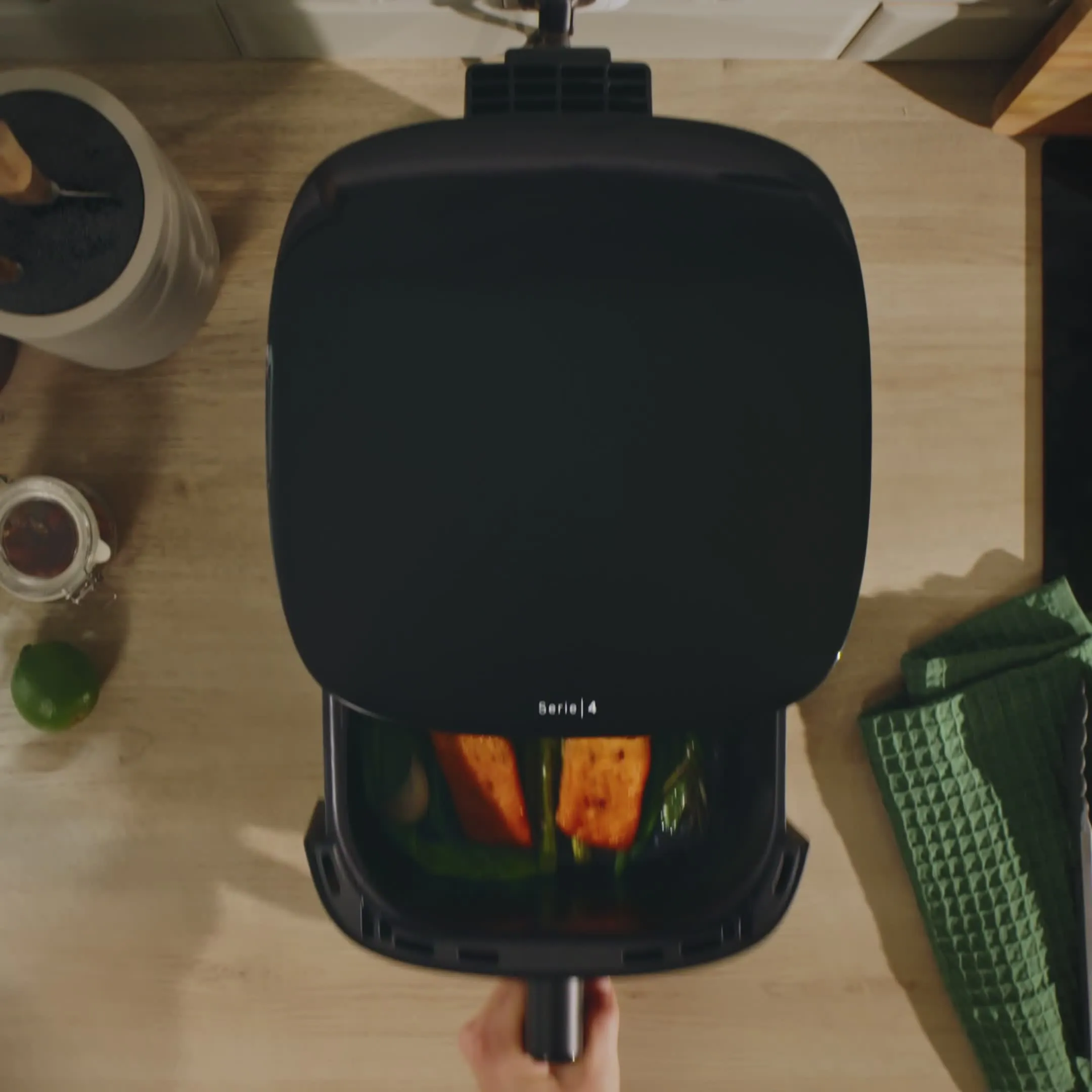 Ovanifrånvy av en svart grillpanna som tillagas av grönsaker på en köksbänkskiva med en grön handduk och lime i närheten.