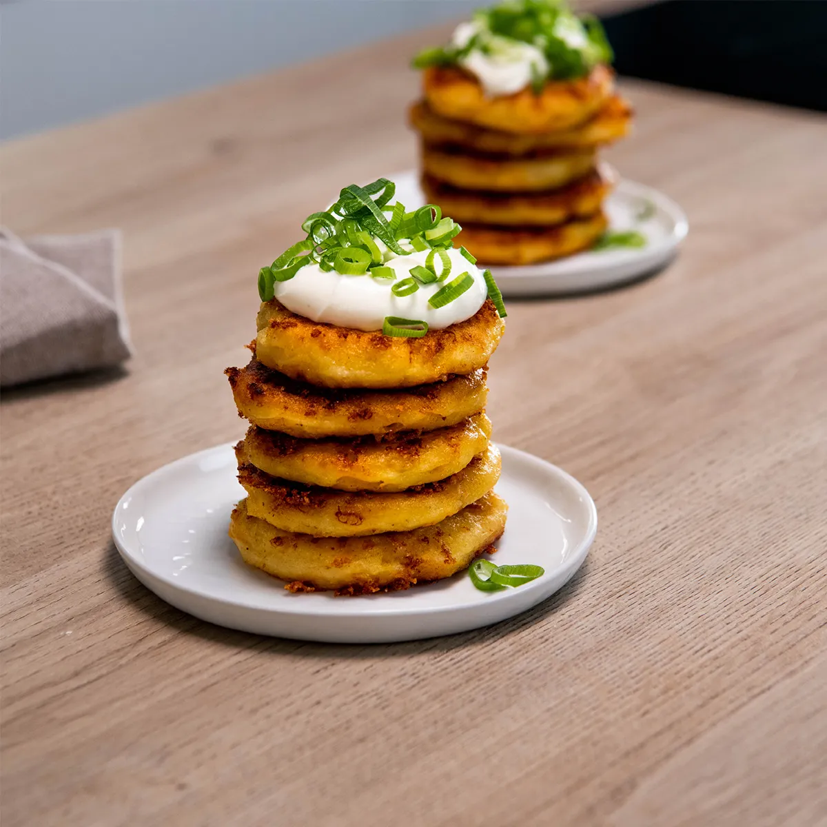Stack of five golden fried fritters on a small white plate, topped with a dollop of sour cream and sliced green onions.