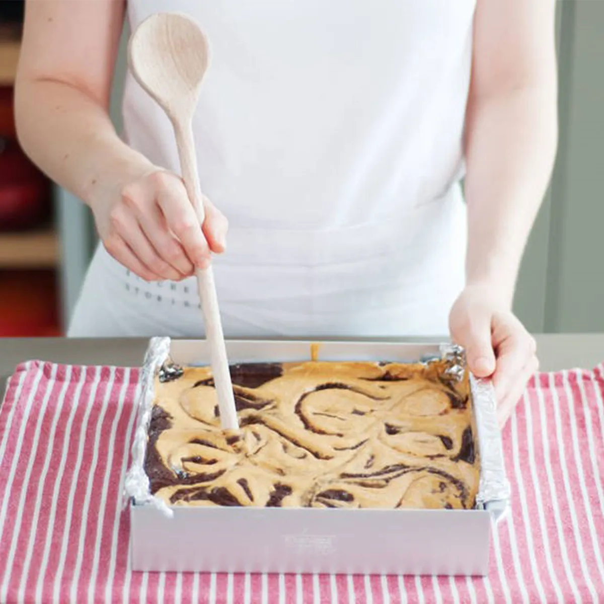 Swirling pumpkin mixture into brownie batter with a spoon before baking in the oven until set and cooled
