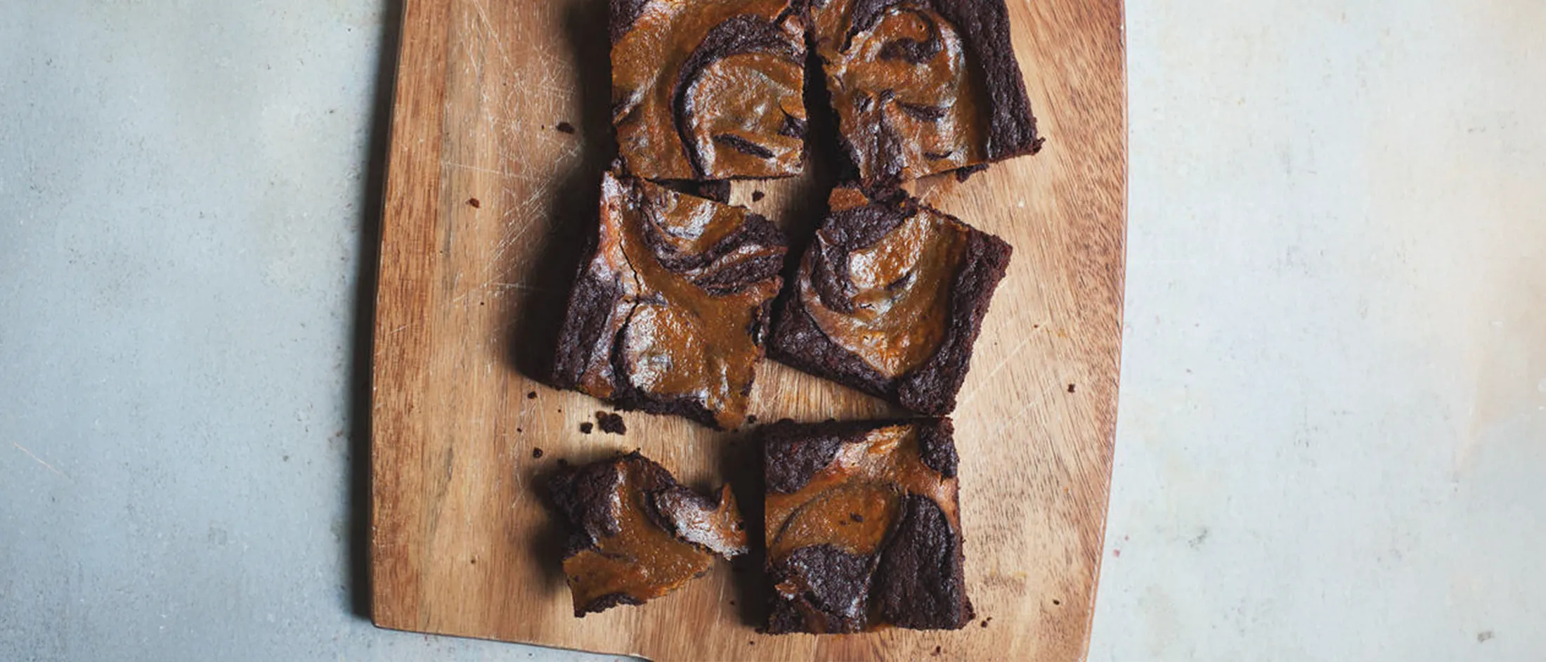 Five chocolate and peanut butter swirl brownies on a wooden cutting board, with one broken piece