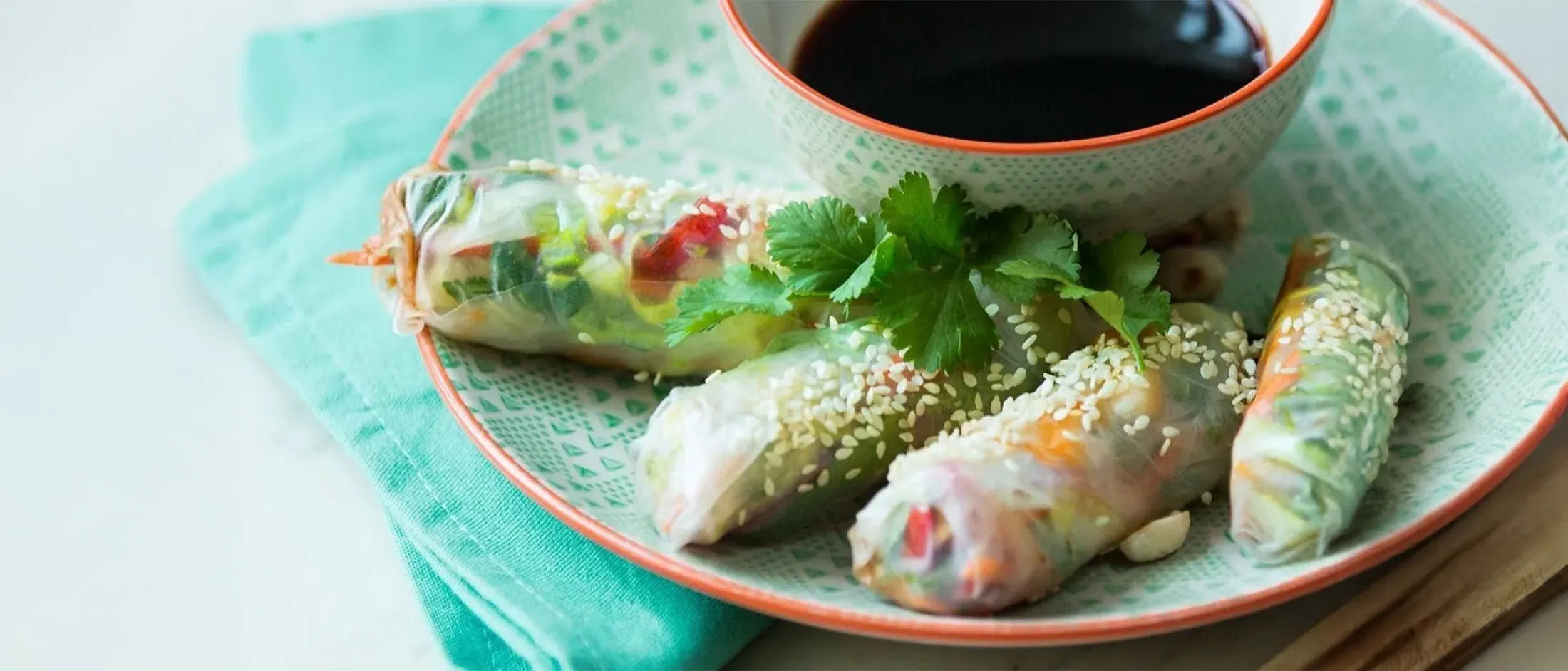 Hands folding a translucent rice paper wrapper around a filling of shredded vegetables on a wooden surface.