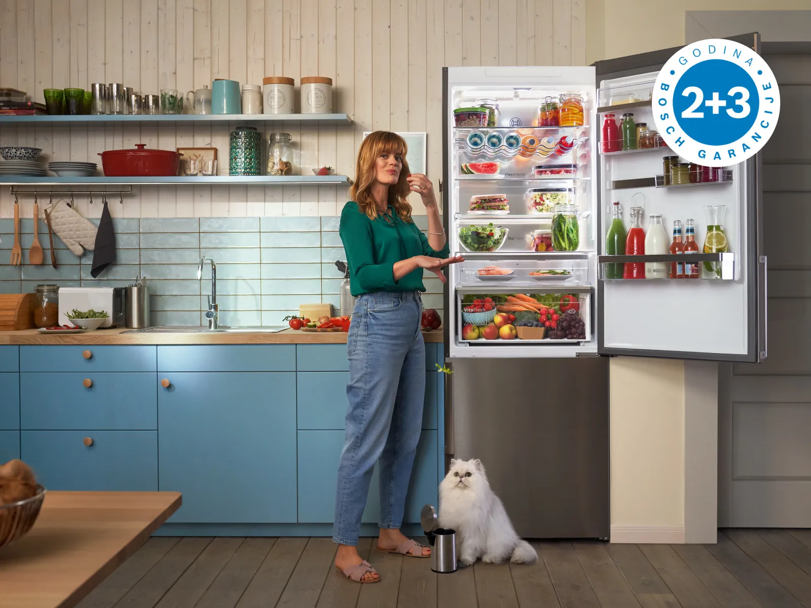 Žena u modernoj kuhinji pored otvorenog frižidera punog namirnica