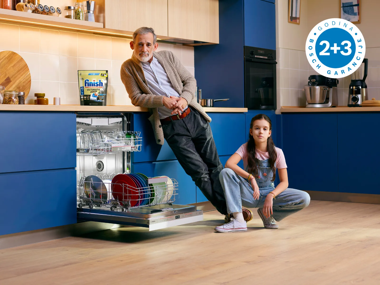 Čovek i dete u modernoj plavoj kuhinji pored mašine za sudove