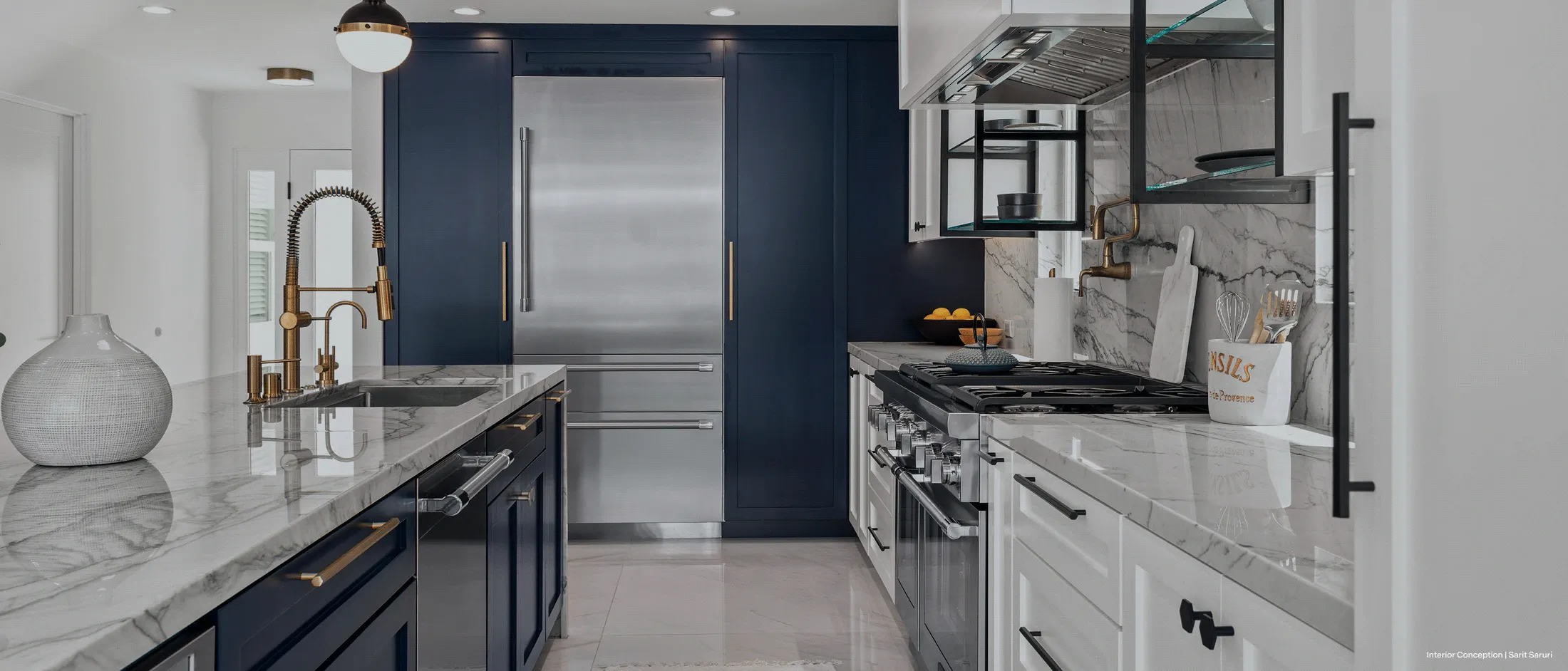 Modern kitchen with navy blue cabinets, marble countertops, gold fixtures, stainless steel appliances, and open shelving.