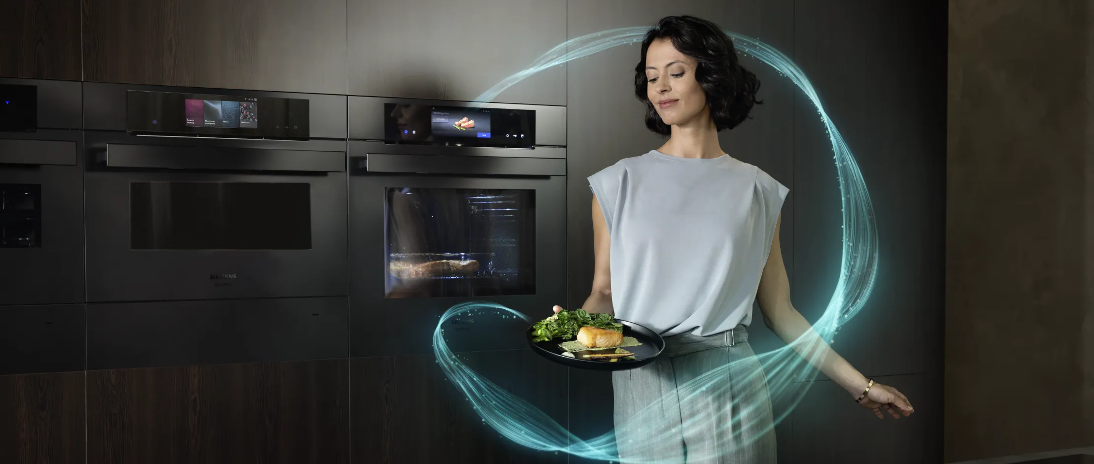 Persona che tiene in mano un piatto con salmone cotto e verdure in una cucina moderna dotata di forni intelligenti integrati.