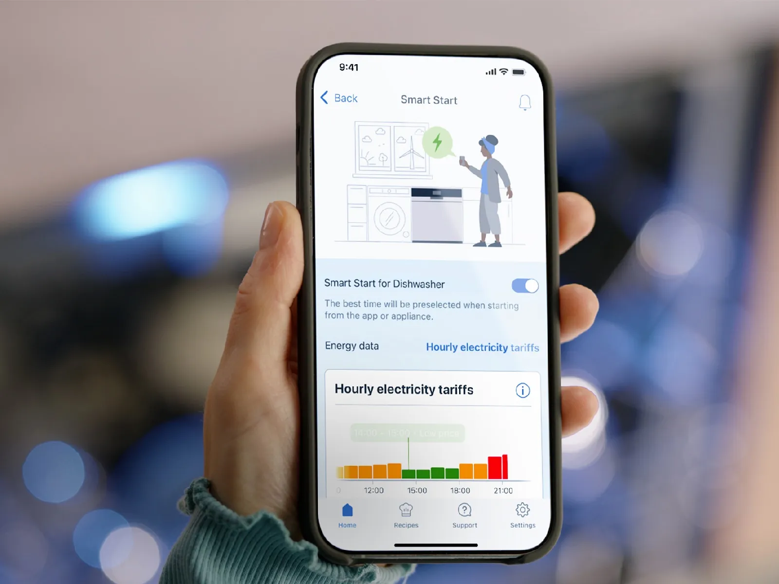 Eine Hand hält Smartphone vor einem geöffneten Geschirrspüler im Hintergrund.