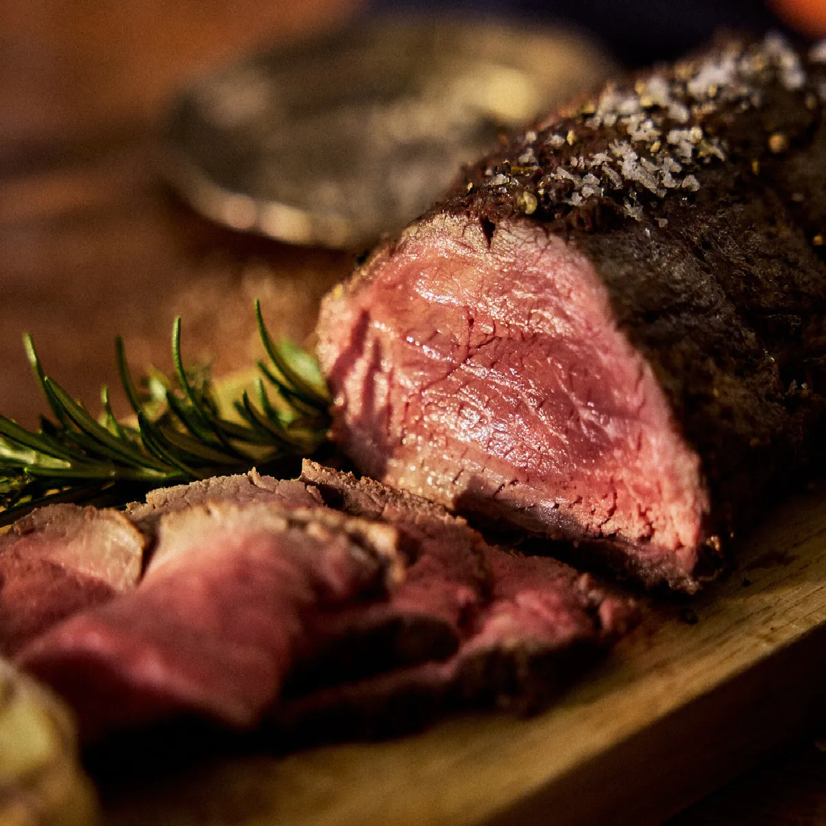 Juicy, bistecca media rara con guarnizione di rosmarino su tagliere di legno.