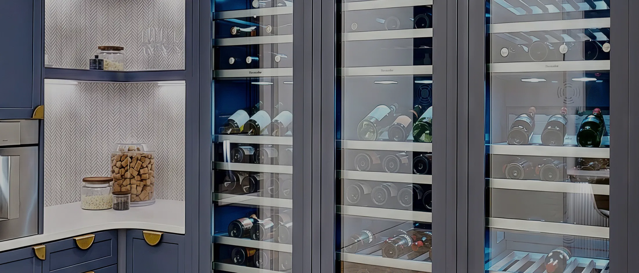 Tall modern wine cooler with glass doors displaying multiple wine bottles on horizontal racks. Navy cabinetry surrounds the cooler.