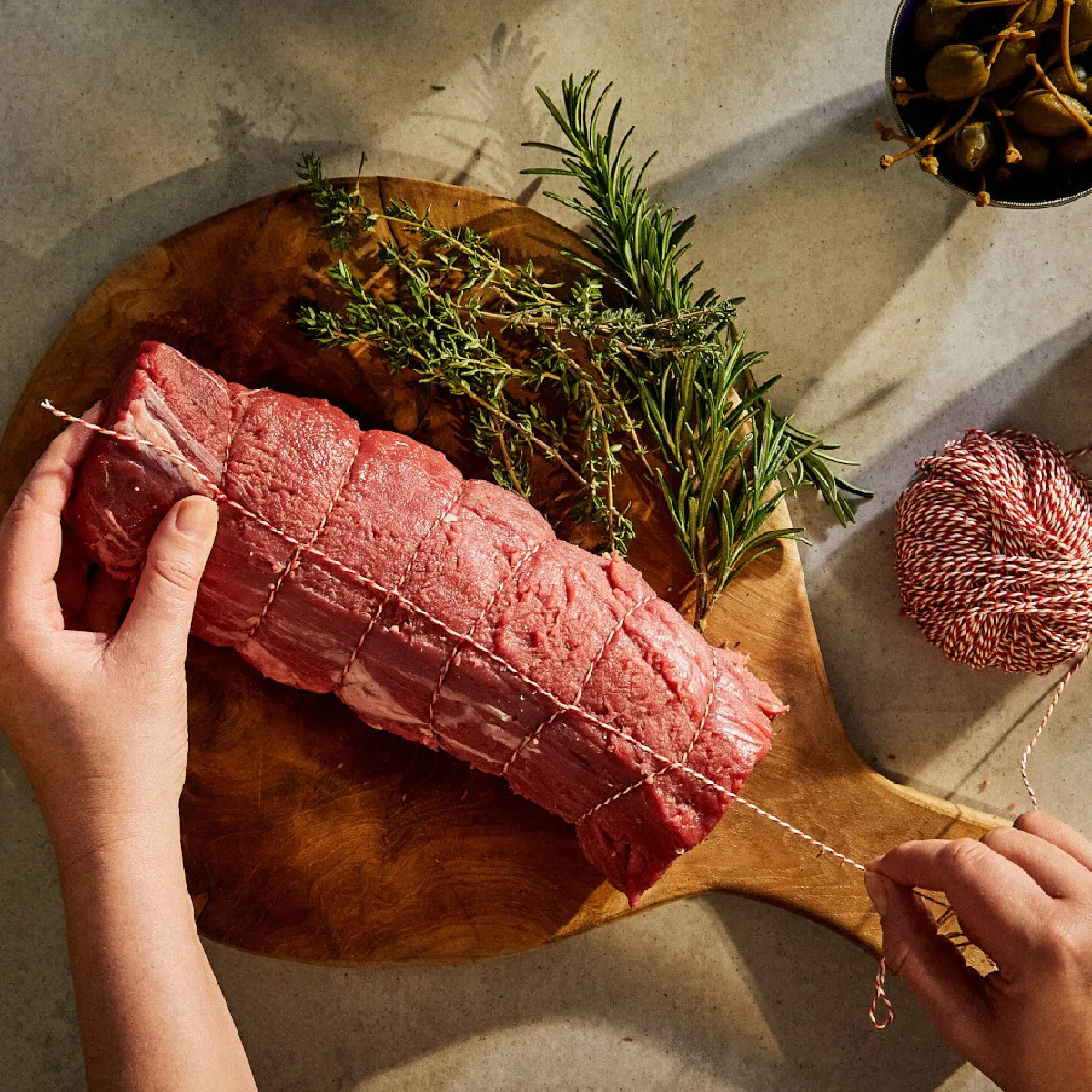 Preparazione di un piatto di carne salata con erbe fresche, spezie e agrumi su un tagliere di legno.