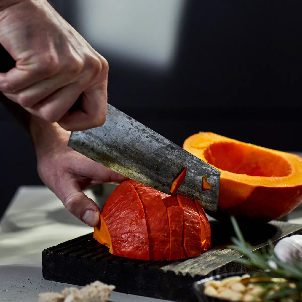 Una persona che affetta una zucca di un arancione brillante su un tagliere in cucina.
