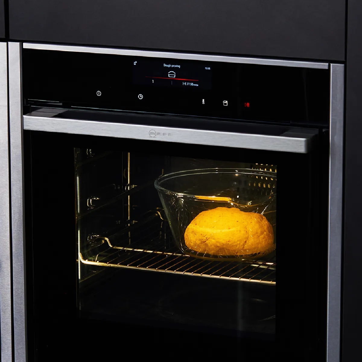 Un forno nero incassato in un mobile da cucina scuro, con il cibo che cuoce all'interno sotto una luce calda.