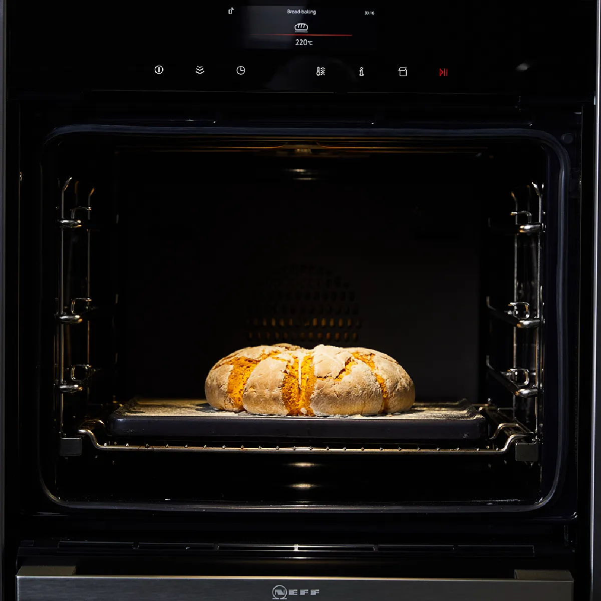 Forno nero incassato con una pagnotta a forma di zucca che si sta dorando su una griglia, illuminata da una luce calda.