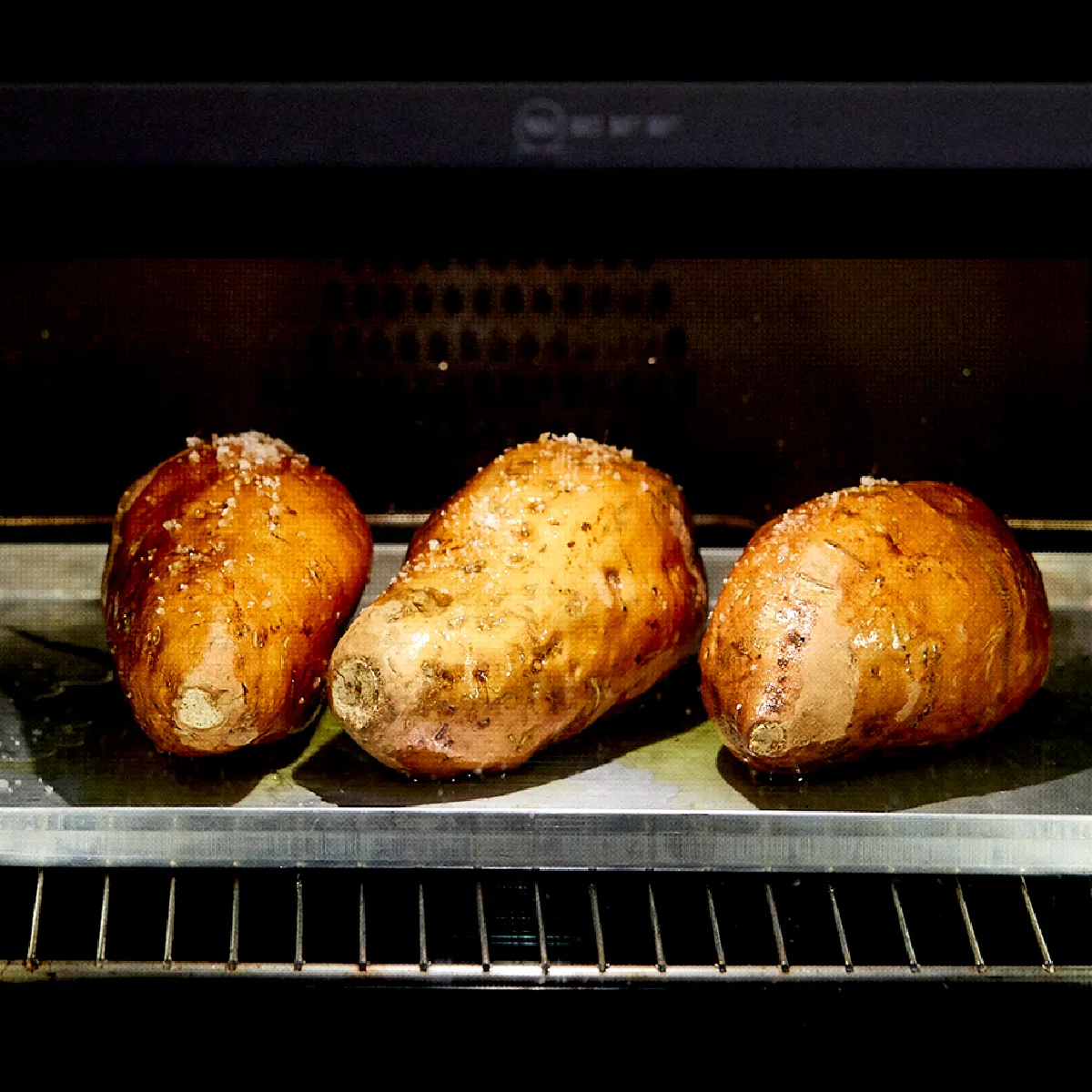 Tre patate al forno su una teglia di metallo in un forno.