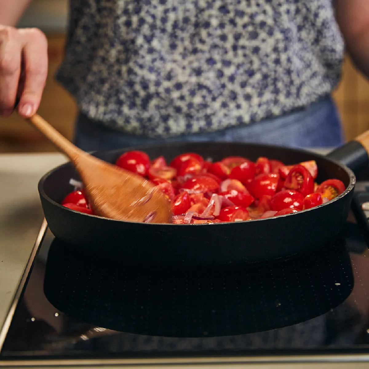 Persona di cucinare pomodori in una pentola su una stufa.