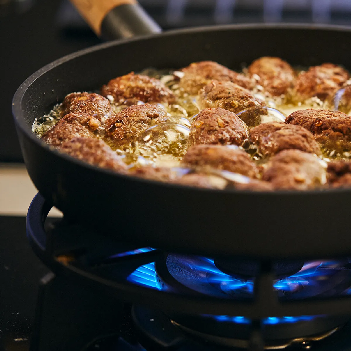 Padella arrosto di carne fritta e verdure su una stufa a gas con fiamme blu.
