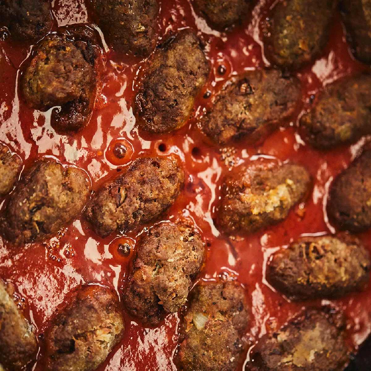 Polpette cucinate in una salsa di pomodoro ricca, servita in una padella scura.