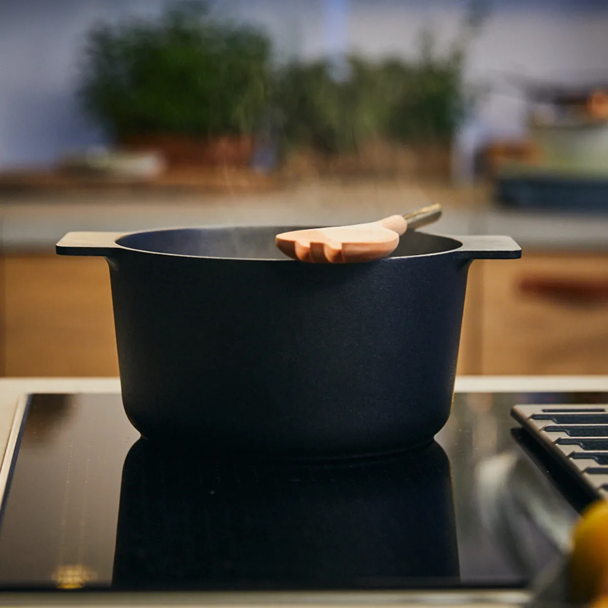 Pentola nera con un cucchiaio di legno appoggiato sopra, posizionata su un piano cottura moderno in una cucina.