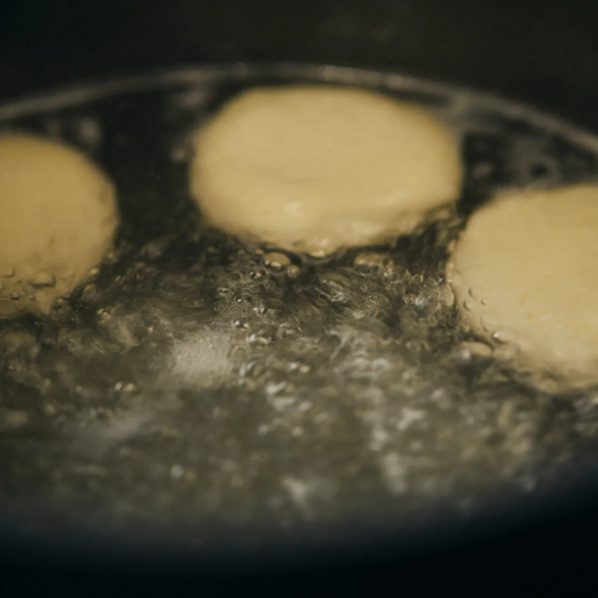 Acqua bollente con gnocchi galleggianti o panini in un vaso scuro.