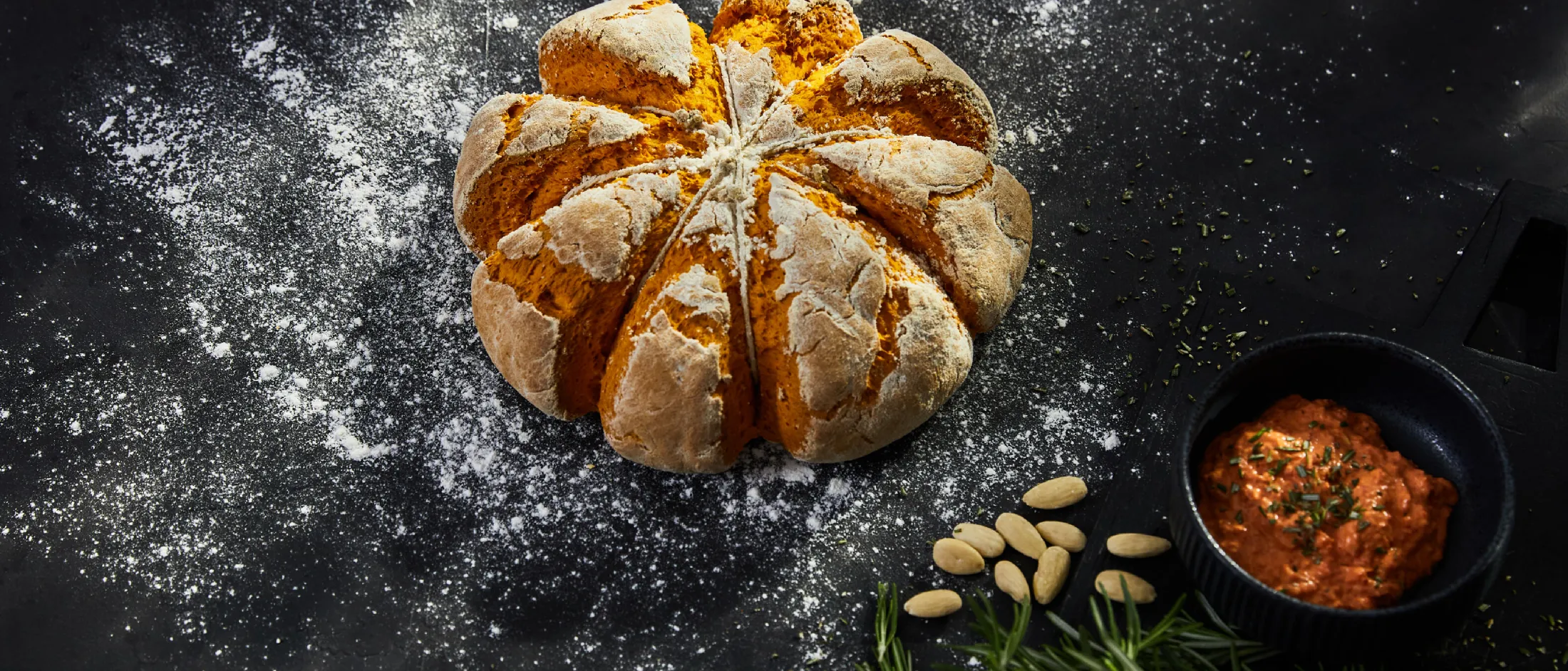 Il pane appena cotto, le spezie, le erbe e una spolverata di farina su uno sfondo scuro.