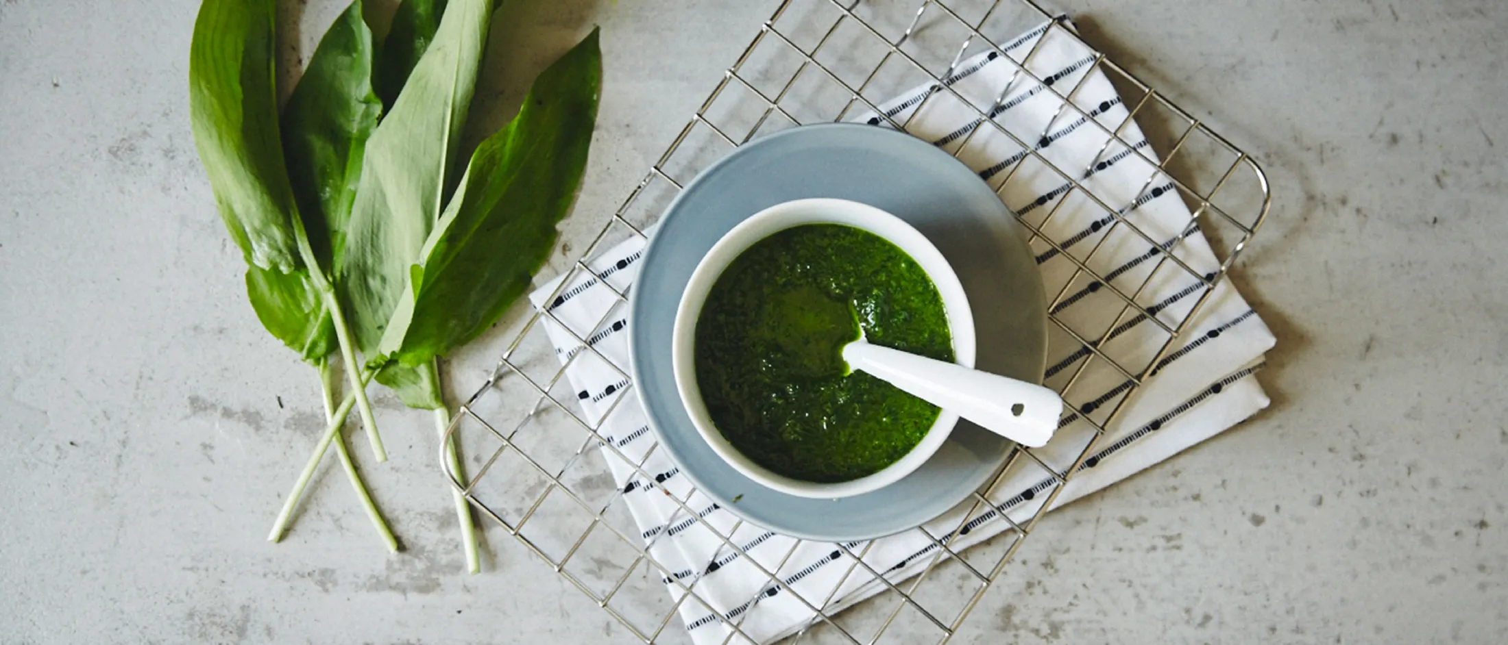 Erbe a foglia verde, una ciotola di salsa verde, e un rack di filo su una superficie leggera.