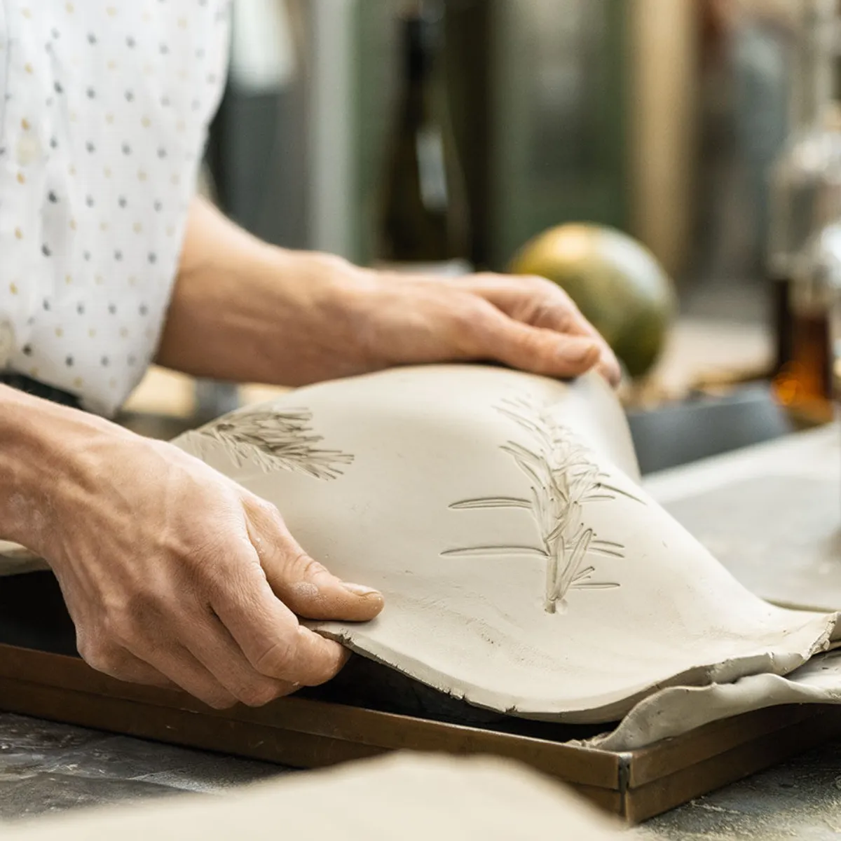 Una persona che solleva una lastra di argilla decorata con motivi vegetali da un telaio di legno in un laboratorio di ceramica.