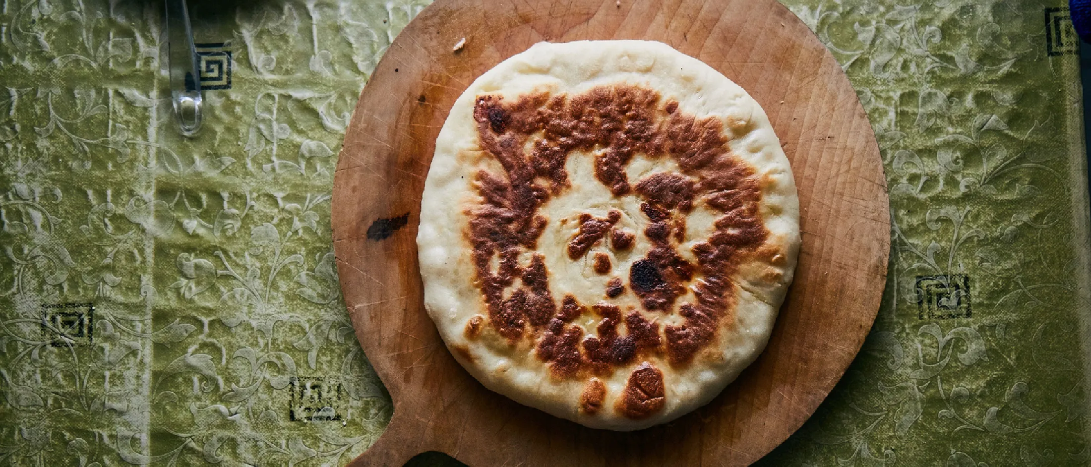 Pane piatto rotondo dalla superficie dorata su un tagliere di legno, sopra una tovaglia verde a motivi.