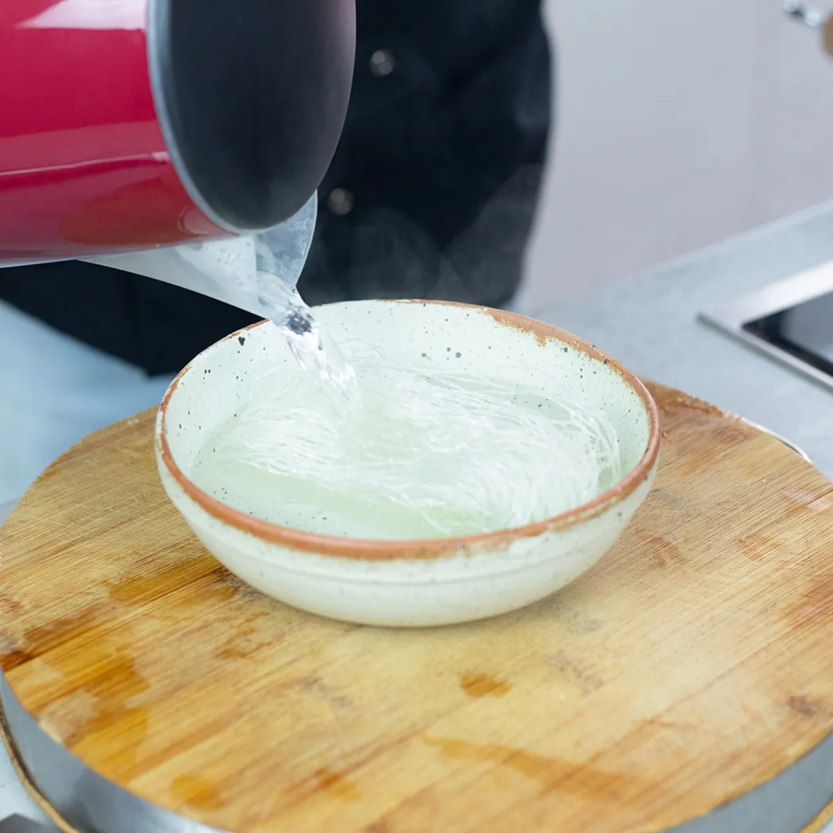Acqua versata da un bollitore rosso in una ciotola bianca su un tagliere di legno.
