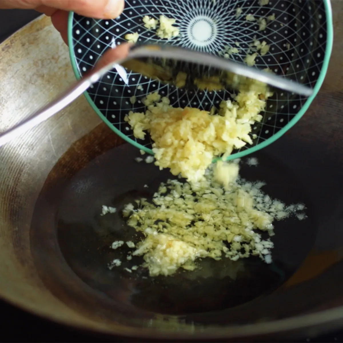 Mani che versano aglio tritato da una ciotola in un wok di metallo