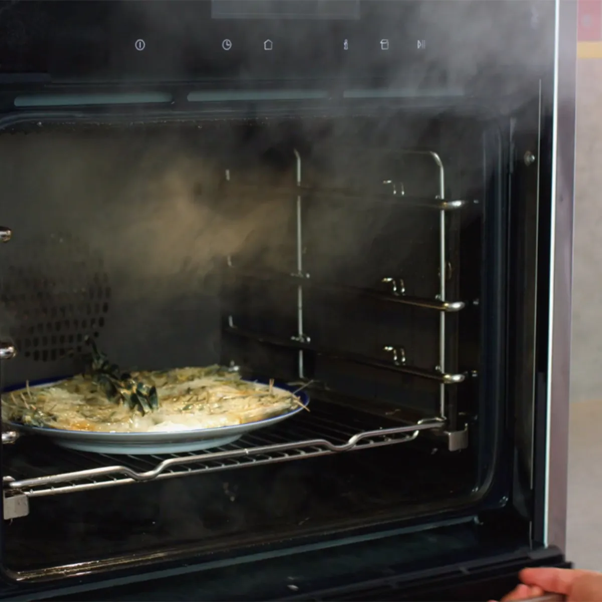 Forno aperto con piatto di vermicelli e gamberi che cuoce al suo interno con vapore visibile.
