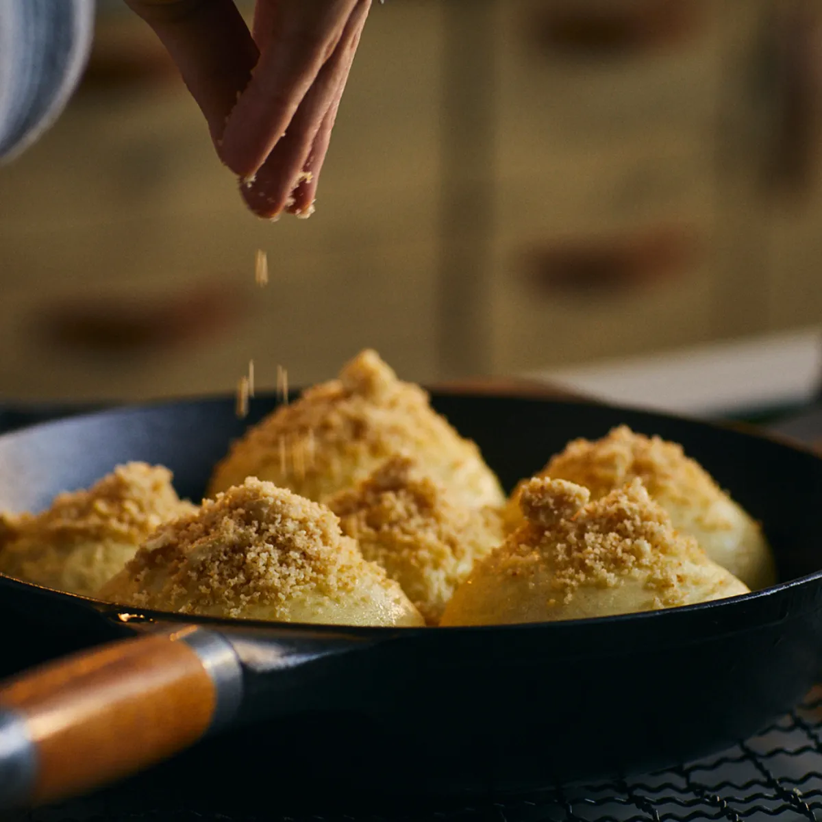 Mano che cosparge pangrattato su gnocchi di pasta in padella con manico in legno.