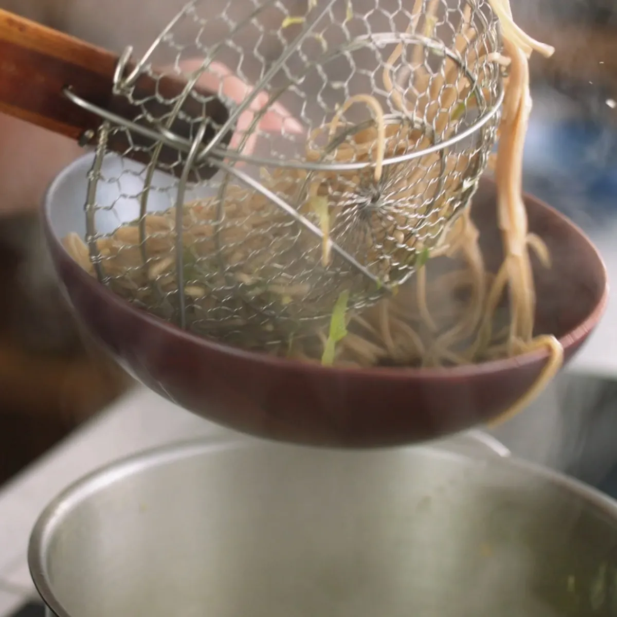 Persona che scola spaghetti con un mestolo a rete sopra una pentola.