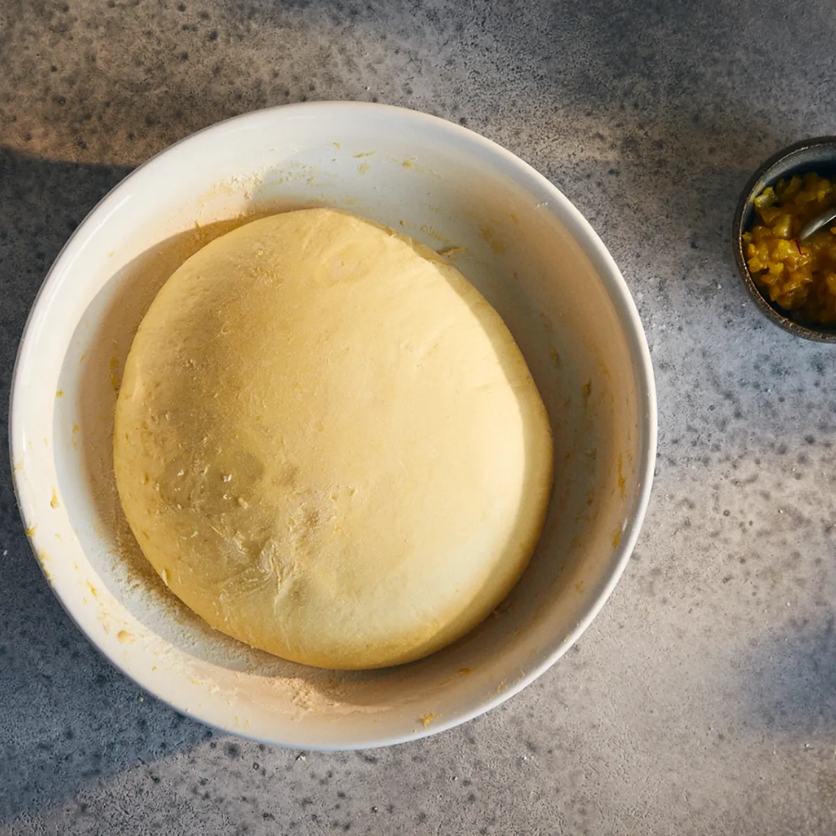 Ciotola con impasto lievitato e ciotolina con ripieno accanto su superficie grigia.