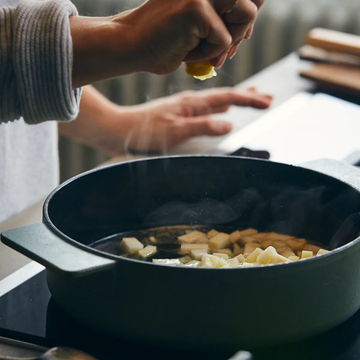 Mano che spremere un limone sopra una padella con cubetti di patate in cottura su piano cottura moderno.