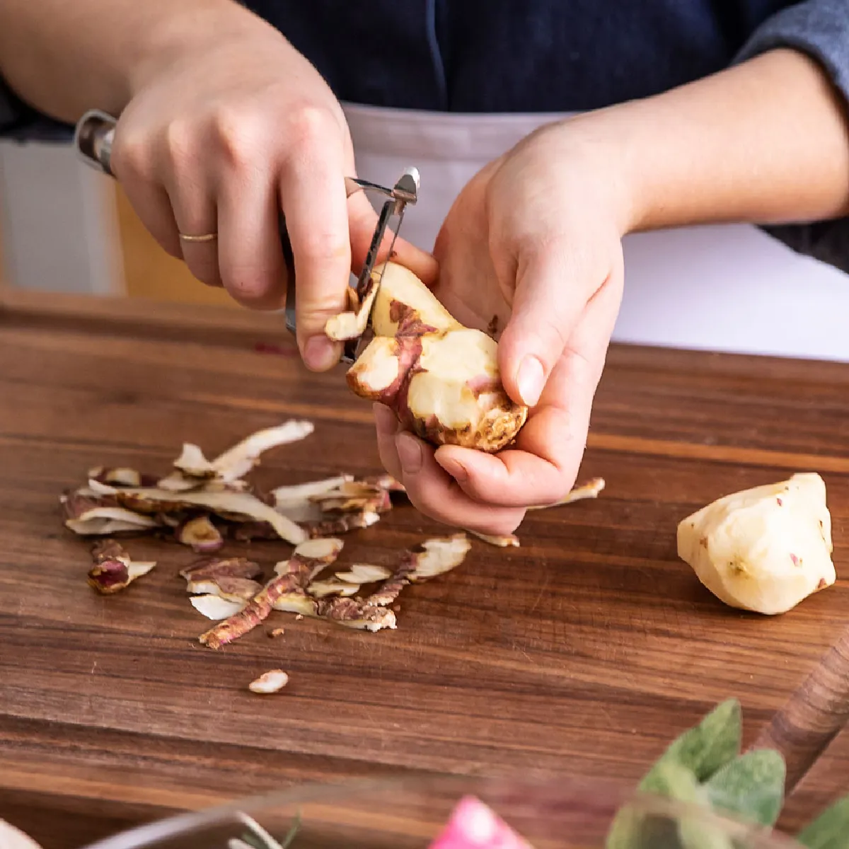 Mani tagliare lo zenzero su un tagliere di legno con varie verdure e utensili da cucina.